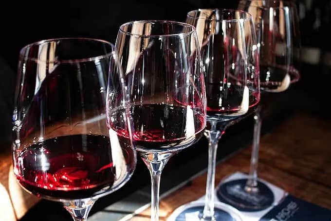 Ett glas rött vin står på ett bord, omgivet av mjukt ljus och förväntansfull stämning.