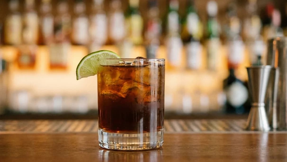 Ett glas Dark 'n' Stormy-cocktail med lime och mynta garnering på en mörk bakgrund.