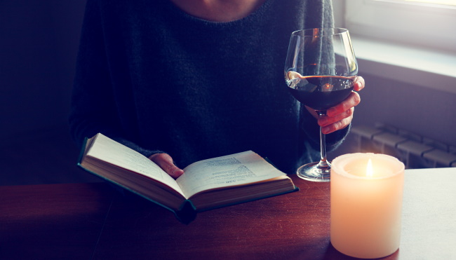 vinböcker - en kvinna läser en bok och har ett glas vin i handen